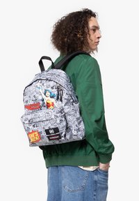 Mochila con un estampado de cómic en blanco y negro de Wonder Woman, detalles en rojo y amarillo, y parches con logotipos. La tela es duradera y con textura.