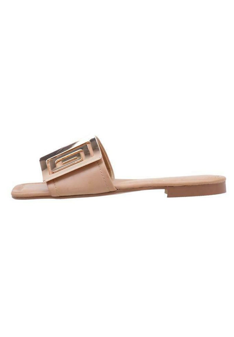 Sandalía plana beige hecha de material sintético suave, con una correa ancha y una hebilla decorativa en tono dorado en la parte superior.