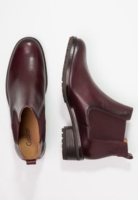 Burgundy nahka nilkkurit, joissa on joustavat sivupaneelit, teksturoitu kumipohja ja matala lohkopohja, varustettuna lenkillä, joka helpottaa pukemista.