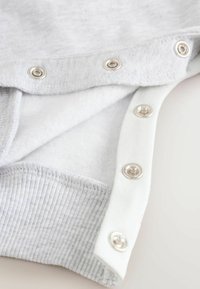 Világosszürke ruhadarab puha, bolyhos belsővel; ezüst színű patentgombokkal a fehér gallér széle mentén és bordázott szegély textúrával.
