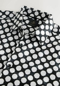 Lühikeste varrukatega must-valge särk geomeetrilise kuue nurga mustriga, valmistatud sileda kangaga, millel on terav kaelus ja nööbid.