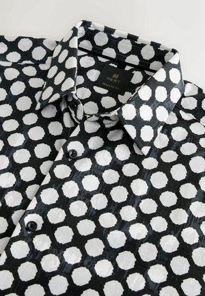 Cămașă cu mânecă scurtă în alb și negru, cu un model geometric de hexagoane, realizată dintr-un material neted, având un guler ascuțit și nasturi.