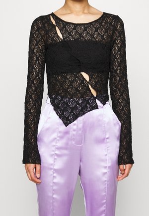 Top nero in pizzo a maniche lunghe con design a tagli, realizzato in tessuto testurizzato e con dettaglio a torsione, abbinato a pantaloni in satin lilla.
