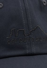 Ciemnoniebieska tkanina z czarnym haftowanym zarysem miasta i napisem „OFF DUTY GEAR” na przednim panelu czapki z daszkiem.