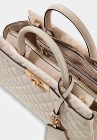 Gequiltete beigefarbene Handtasche mit goldfarbener Hardware, doppelten oberen Griffen und mehreren Innenfächern, mit schwarzem Besatz und Logo-Detail.