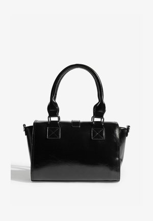 Musta lakattu nahkalaukku pyöreillä kahvoilla, suorakulmaisella rungolla ja kulmikkailla yksityiskohdilla laukun päissä. Varustettu irrotettavalla olkahihnalla.