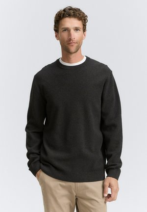 Suéter de punto gris oscuro con cuello y puños acanalados, combinado con pantalones beige claros; textura suave y corte regular.