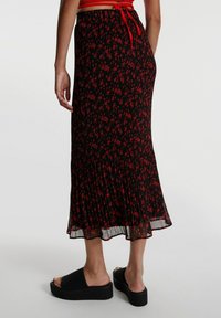 Femme portant une jupe midi plissée noire à motif floral rouge et des sandales à plateforme noires, vue de dos.