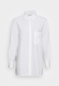 Chemise blanche à manches longues en coton, avec un col classique, une fermeture bouton et une poche poitrine du côté gauche. Texture lisse.