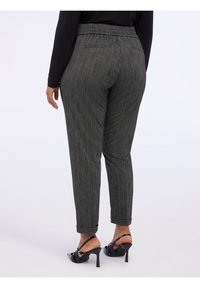 Harmaat raidoitetut housut joustavalla vyötäröillä, kapeneva leikkaus ja käärityt lahkeet, yhdistettynä mustiin korkokenkiin.