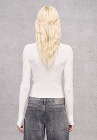 Top bianco a maniche lunghe con coste abbinato a jeans grigi sbiaditi a vita alta, dotati di quattro tasche e etichetta del marchio sul retro.