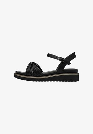 Black sandal with a textured, pleated front strap and adjustable ankle strap. Features a thick wedge sole with zigzag tread.