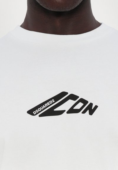 Valge puuvillane T-särk, millel on must logo, mis ütleb "DSQUARED2 ICON", ümar kaelus ja lühikesed varrukad.