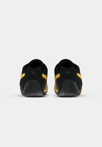 Scarpe sportive nere e gialle con una suola in gomma testurizzata, caratterizzate da una tomaia liscia e accenti gialli a contrasto lungo i lati.
