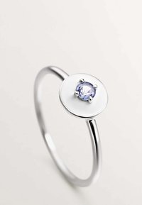 Anillo de plata con un disco redondo de esmalte blanco y una gema central de color púrpura claro sostenida por cuatro garras. Diseño de banda lisa.