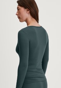 Langsleeve shirt in donker teal, gemaakt van zacht materiaal, met een ronde halslijn en een slim fit. Gladde textuur zonder zichtbare patronen.