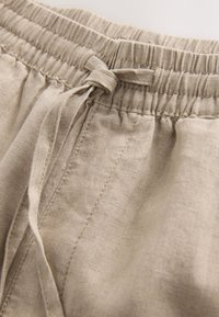 Shorts in lino beige chiaro con vita elasticizzata e dettaglio a coulisse. Presentano una texture liscia e cuciture visibili lungo le cuciture.