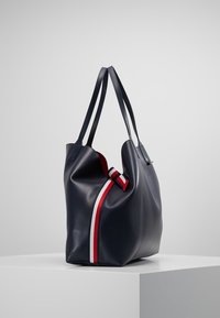 Granatowa skórzana torba na ramię z dwiema ramiączkami, z białym i czerwonym paskiem po jednej stronie oraz gładką teksturą.