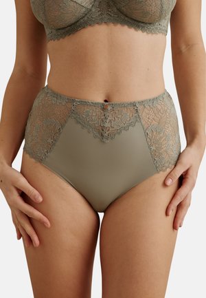 Soutien-gorge en dentelle verte et culotte taille haute avec panneaux en dentelle florale portés par une femme, les mains posées sur les cuisses.