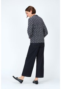 Blusa a righe bianco e nero con maniche lunghe e vestibilità rilassata, abbinata a pantaloni in denim a gamba larga scuri e mocassini neri.