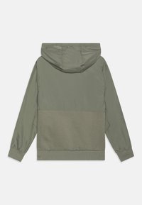 Casaco com capuz em verde-oliva com um design em dois tons. Apresenta uma parte superior lisa e uma bainha texturizada e canelada. Possui punhos elásticos.