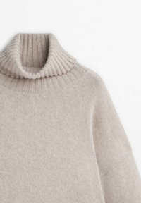 Beige polotröja med ribbad krage och mjuk textur. Designen inkluderar sänkt axel och en lös passform.