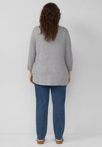 Szary longsleeve z luźnym krojem, z zaokrąglonym dołem. Połączony z niebieskimi dżinsami i jasnobrązowym obuwiem.