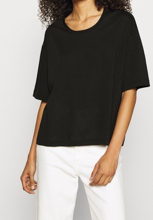 Musta lyhythihainen T-paita pyöreällä pääntielle, valmistettu pehmeästä puuvillakankaasta. Löysä malli suoralla helmalla, yhdistetty valkoisiin housuihin.