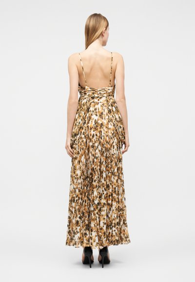 Γυναίκα που φοράει μακρύ, πλισέ φόρεμα με animal print, λεπτές τιράντες και ανοιχτή πλάτη, συνδυασμένο με μαύρα ψηλοτάκουνα, όρθια με την πλάτη στραμμένη.