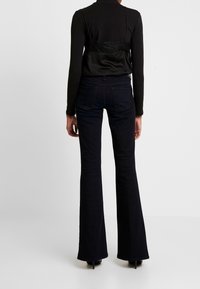 Svart långärmad topp med spetsdetalj på ryggen, kombinerad med mörka utsvängda jeans. Båda plaggen är figurnära och släta i texturen.