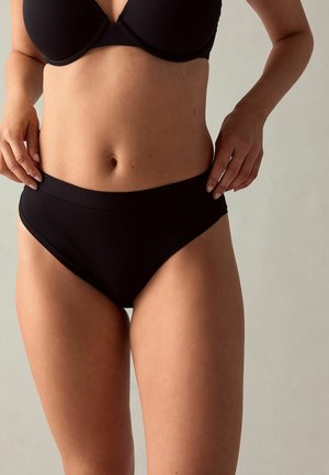 Zwarte hoogsluitende onderbroek met een brede elastische tailleband, een gladde textuur en een minimalistisch ontwerp. Geen zichtbare patronen of hardwaredetails.