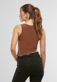 Brun ribbad linne med vågformad nederkant och dekorativa nitar längs kanten, ihop med svarta högmidjade jeans.