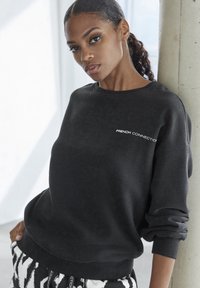 Black sweatshirt with crew neck, relaxed fit, featuring "FRENCH CONNECTION" in white on the chest. Textured fabric, long sleeves, ribbed cuffs.