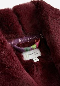 Burgundijas mākslīgā kažokāda ar mīkstu tekstūru. Iekļauts daudzkrāsains pakaramais un kopšanas etiķete ar "b by Ted Baker" zīmolu.