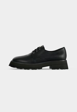 Chaussure en cuir noire à lacets avec semelle épaisse à relief et petit talon, vue de côté sur un fond clair uni.