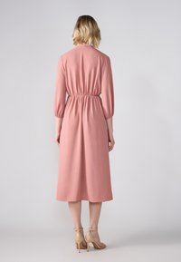 Støvet rosa midi-kjole med samlet midje, trekvartlange ermer og glatt tekstur. Kombinert med nude høyhælte sandaler.