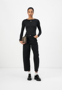 Black long-sleeve top with a square neckline and small logo, paired with loose black denim pants. Black platform shoes and a small brown bag.