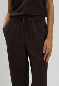 Donkerbruine, lichtgewicht broek met een elastische tailleband en trekkoord, voorzien van zijzakken en een gladde textuur.