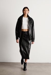 Μαύρο δερμάτινο μπουφάν με κουκούλα, συνδυασμένο με εφαρμοστό λευκό crop top, ψηλόμεση μαύρη δερμάτινη φούστα και μποτάκια μέχρι τον αστράγαλο. Λείος υφασμάτινος χαρακτήρας και μινιμαλιστικός σχεδιασμός.