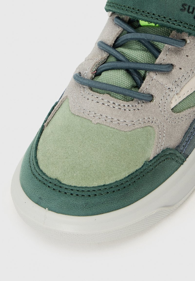 Sneaker in einer Kombination aus hellgrauem Wildleder und grünen Akzenten, mit strukturierten Stoffpaneelen und einer Gummisohle. Grüne Schnürsenkel.