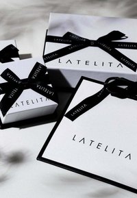 Scatole regalo bianche e borsa con nastri neri, con il marchio "LATELITA" in nero. Le scatole variano in dimensione, con texture liscia e bordi nitidi.