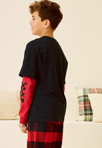 Czarny i czerwony longsleeve pod krótkim czarnym t-shirtem z obrazkiem w kratkę na rękawach, w połączeniu z spodniami w kratę.