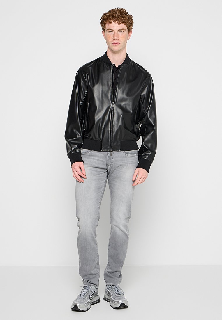 Czarna błyszcząca kurtka bomberka z zamkiem błyskawicznym i ściągaczami, w połączeniu z jasnoszarymi dżinsami i szarymi trampkami. Prosty design z gładką fakturą.