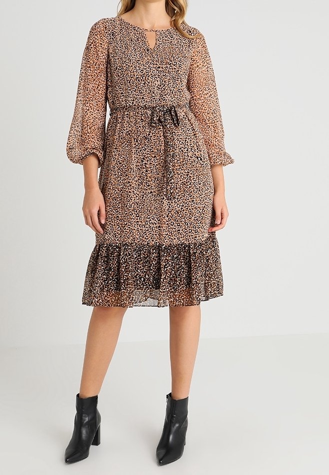 Robe imprimé léopard avec manches longues bouffantes, encolure en goutte d'eau, taille cintrée et ourlet à volants à plusieurs niveaux. Portée avec des bottines noires.