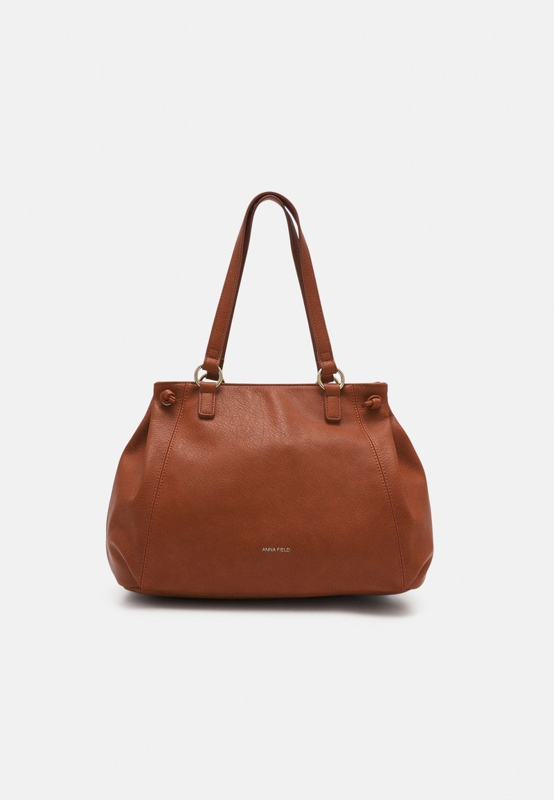 Sac à main en cuir marron avec double bandoulière et logo de marque argenté discret au centre avant, présenté sur fond blanc uni.
