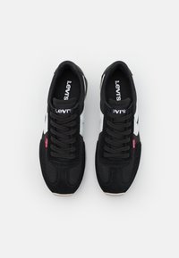 Svarta Levi's sneakers med vita sidsnören, svarta snören och röda Levi's-taggar, sedda ovanifrån på en slät vit bakgrund.