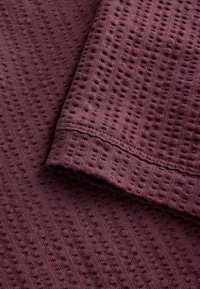Gros plan d’un tissu violet plié avec un motif texturé en forme de gaufre et des coutures visibles.
