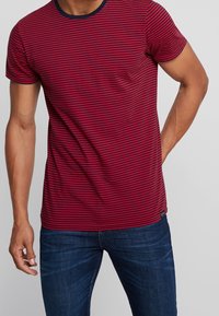 Czerwono-granatowy w paski t-shirt z krótkim rękawem, okrągłym dekoltem i dopasowanym krojem, w połączeniu z niebieskimi dżinsami, z małą metką z logo.
