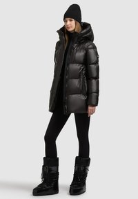 Fekete, fényes felületű puffert dzseki, magas gallérral és kapucnival. Fekete legginggel és térdig érő téli csizmával párosítva.