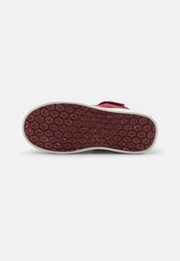 Semelle de chaussure rouge à motif avec une texture hexagonale, dotée d'un bord latéral blanc. La surface présente une légère usure et des accents brillants.